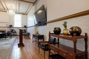 A spacious room with a wooden floor, a large flat-screen TV mounted on the wall, and a decorative table with vases. - The Cape Town Club (Cape Town)