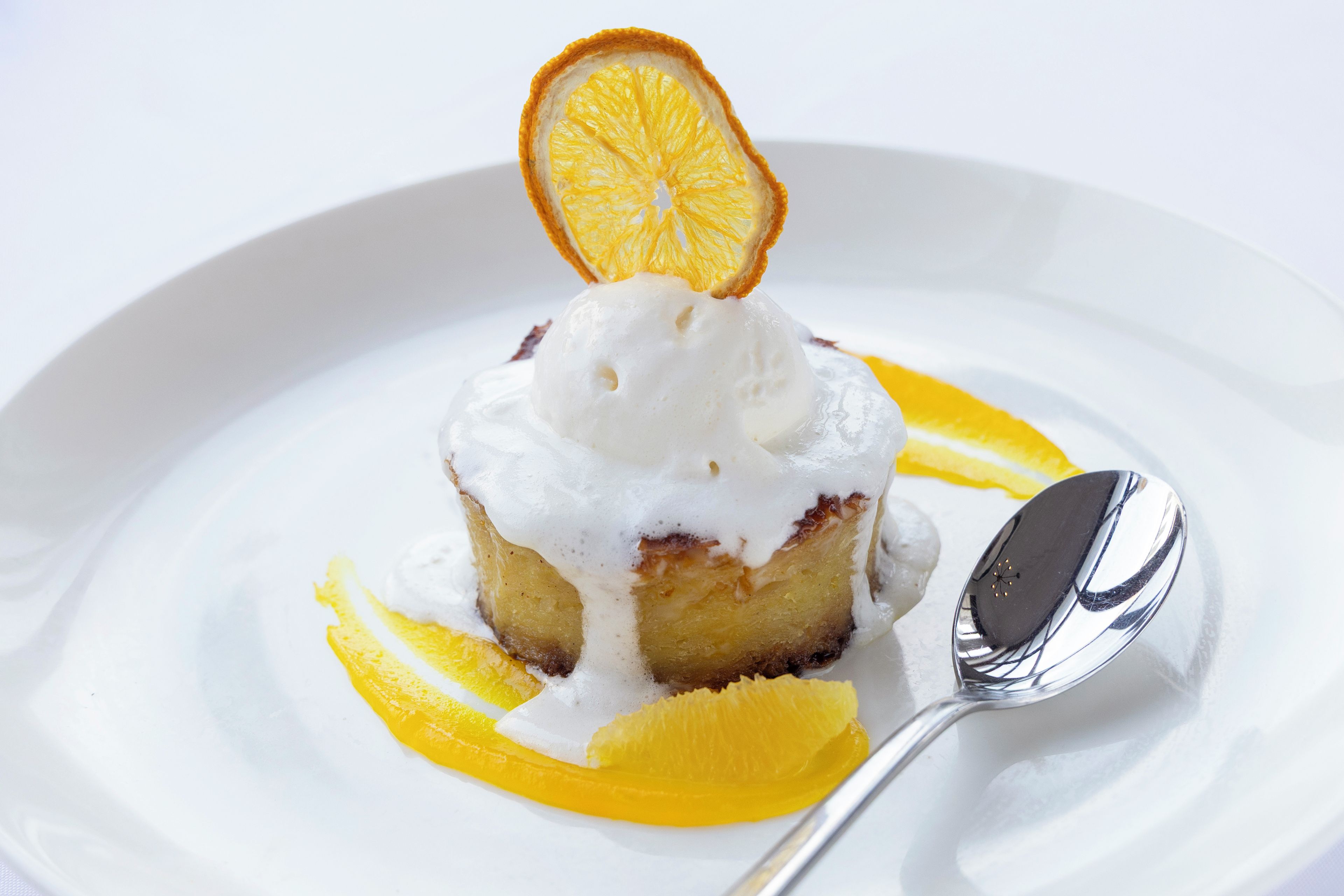 A dessert with a scoop of ice cream on top, served on a white plate with a slice of orange and a spoon.