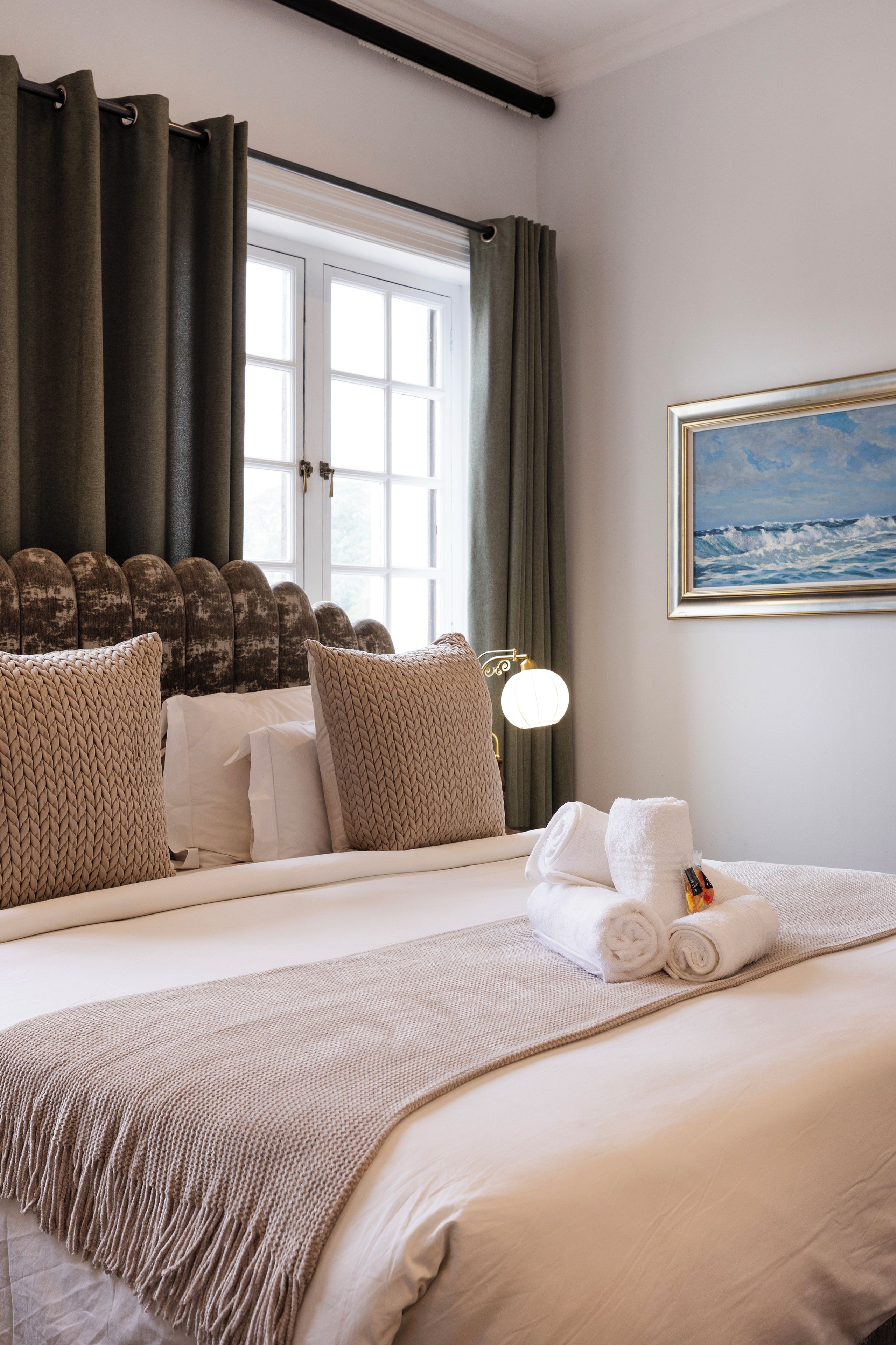 Een hotelkamer met een groot bed, een schilderij van de zee en een raam met gordijnen.