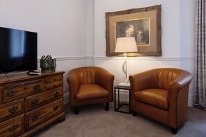 A room with a television on a wooden dresser, two leather armchairs, a lamp, and a framed picture on the wall. - The Cape Town Club (Cape Town)