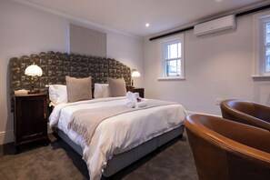 A bedroom with a large bed, two bedside lamps, a brown leather chair, and an air conditioning unit. - The Cape Town Club (Cape Town)