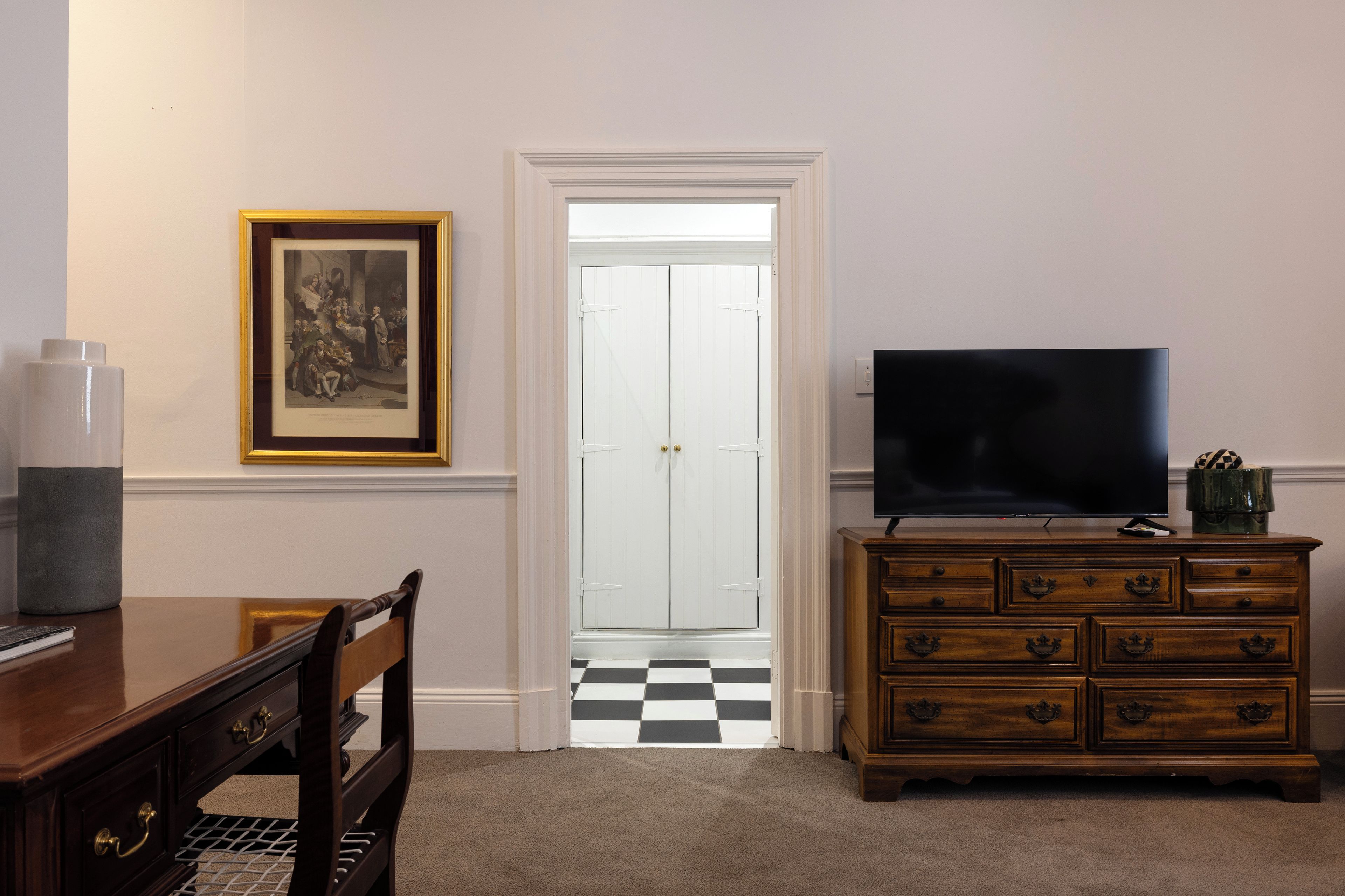 Una habitación con un aparador de madera, un televisor encima, un cuadro en la pared y una puerta que da a un pasillo a cuadros.