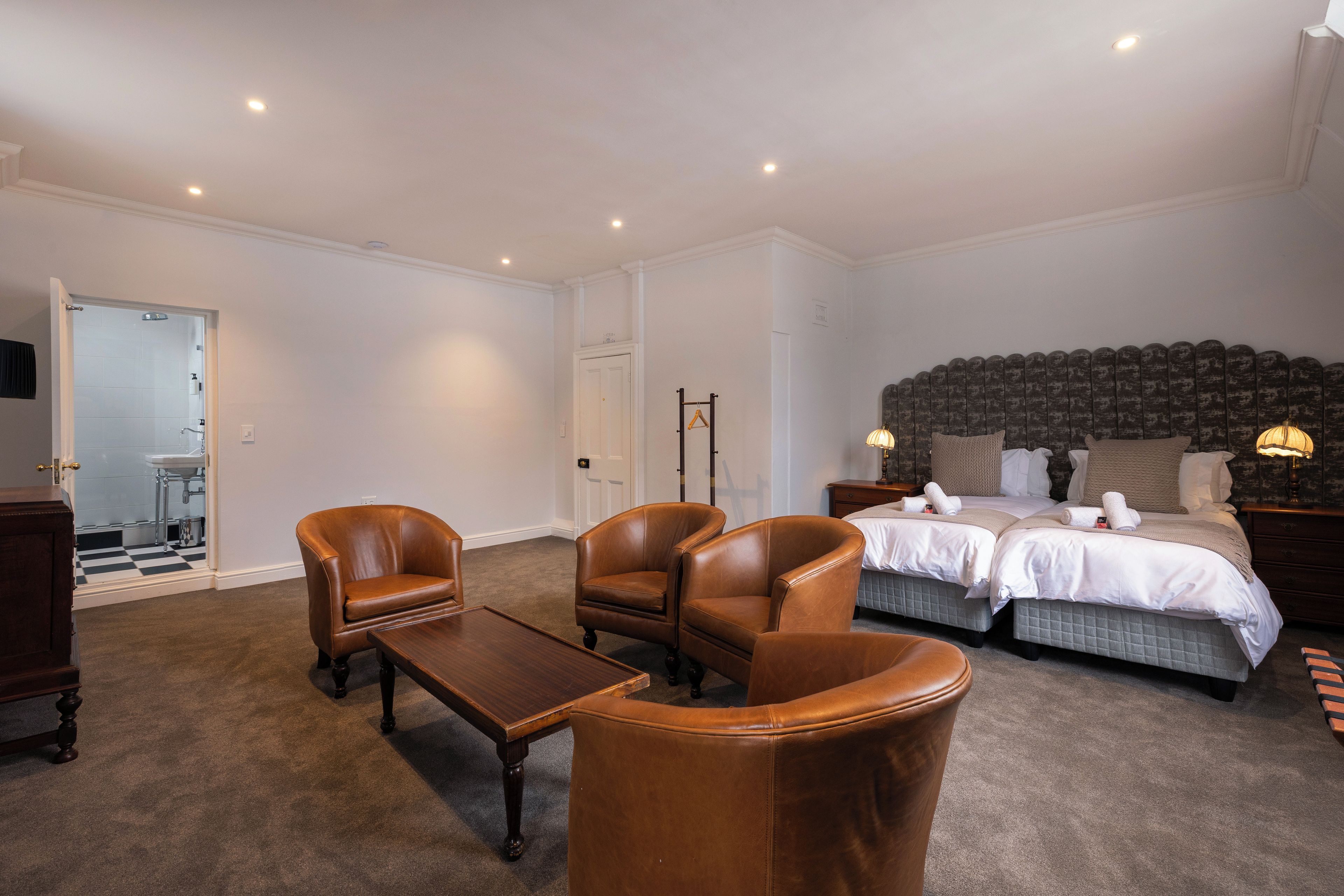 A hotel room with a large bed, two armchairs, a small table, and a mirror.