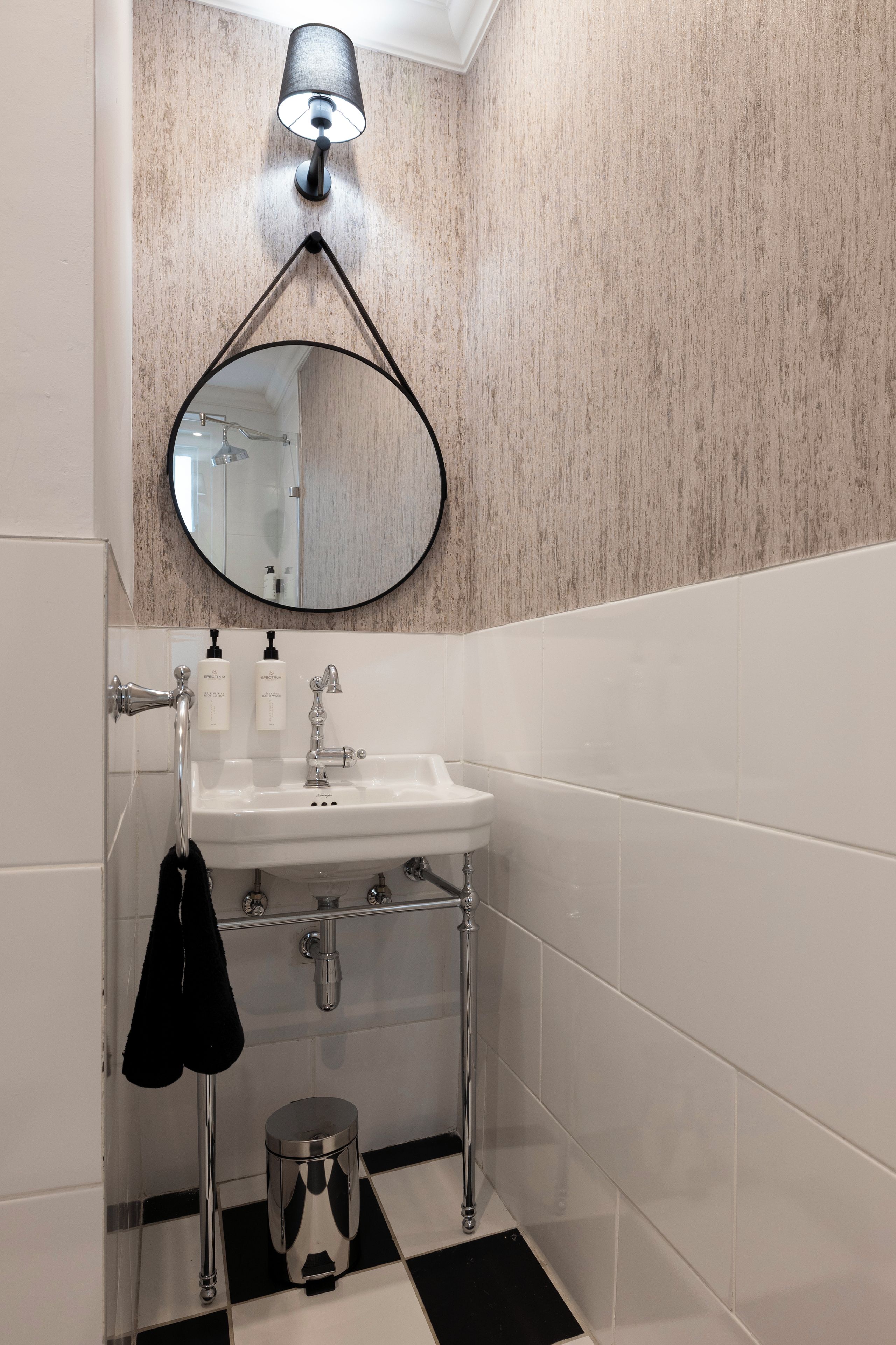 Un baño con un lavabo blanco, un espejo y una toalla negra colgada en un perchero.