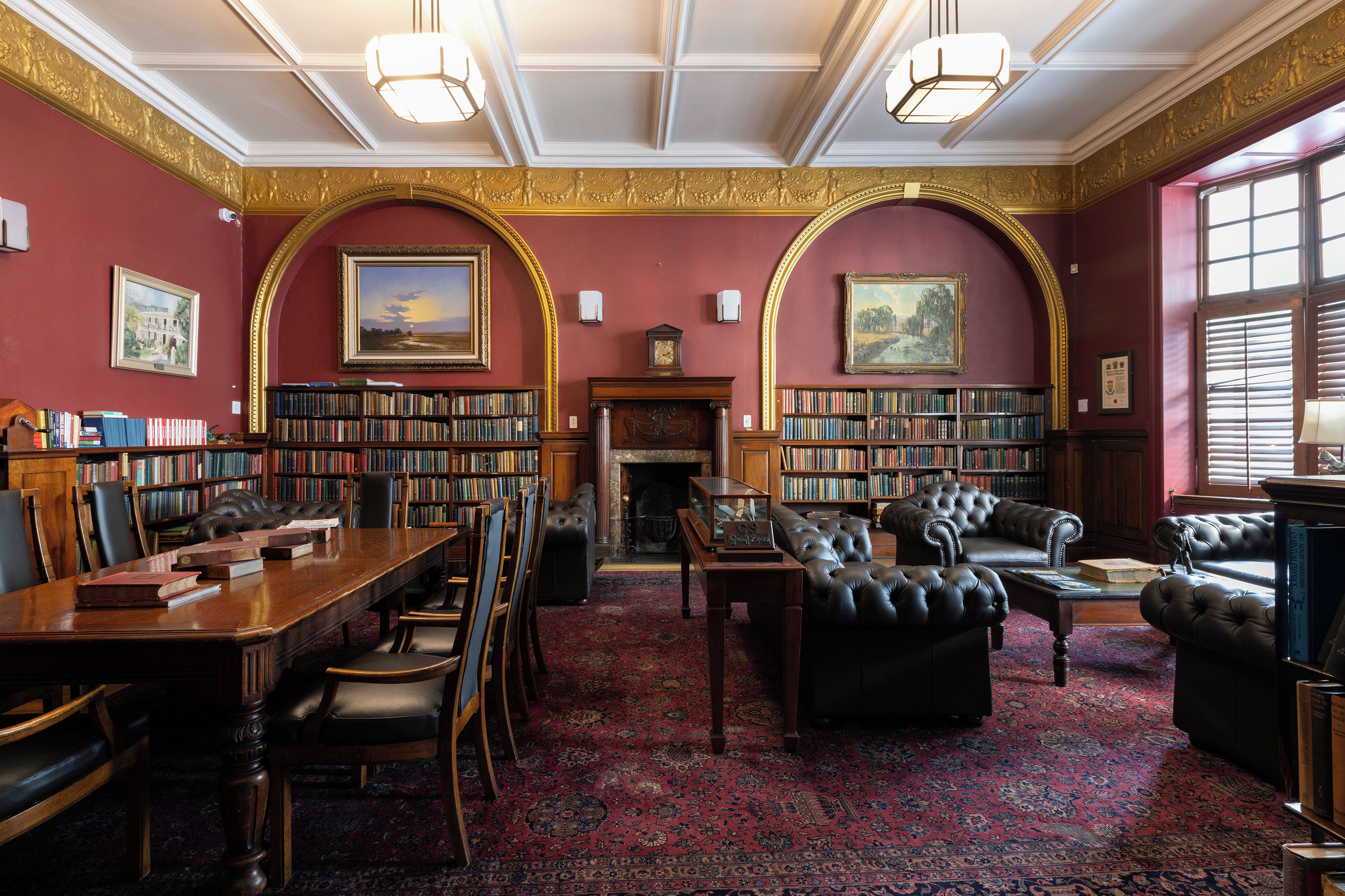 A library with bookshelves, a fireplace, leather furniture, and a patterned carpet.