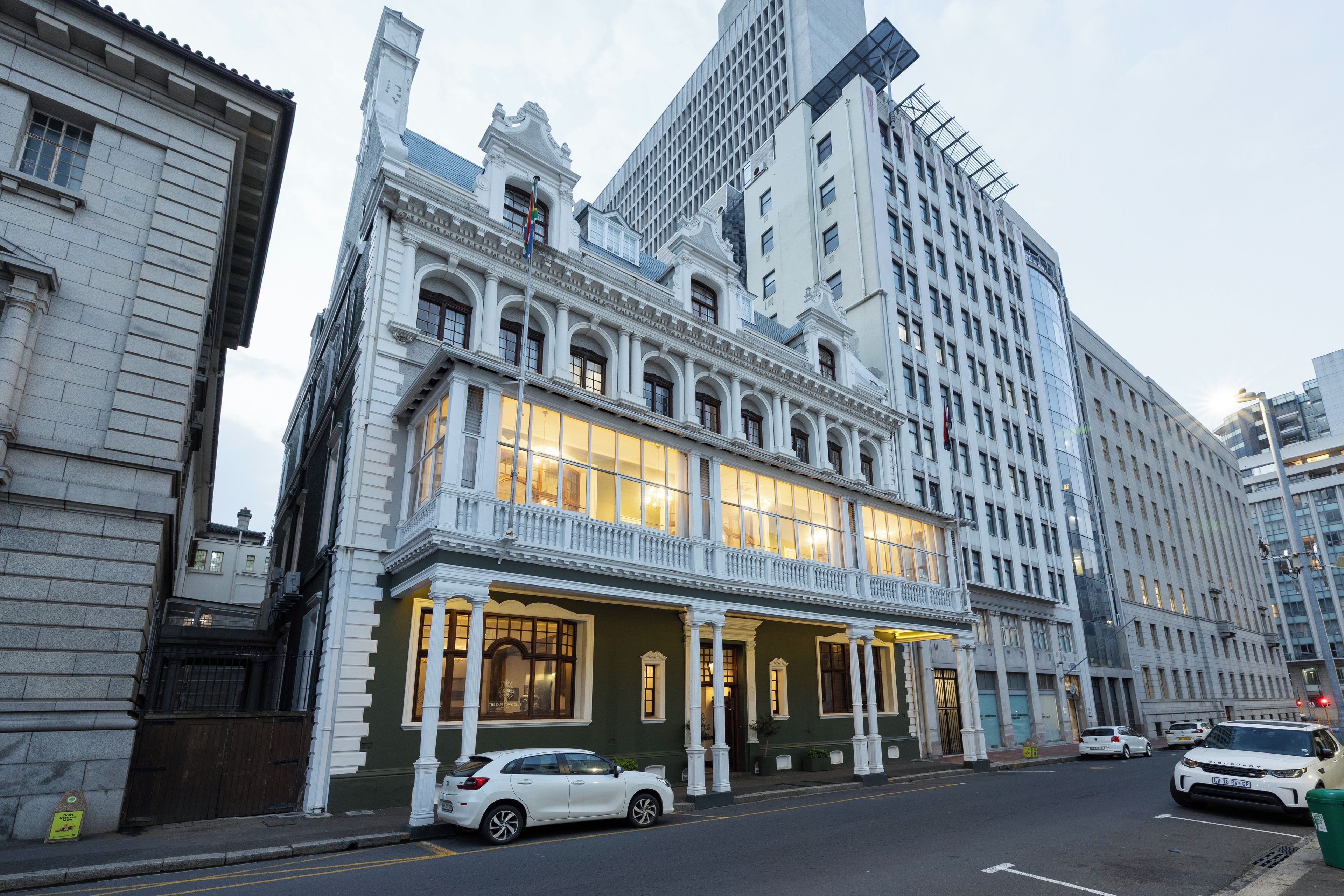 Un edificio histórico con balcón y amplias ventanas, junto a un rascacielos moderno.