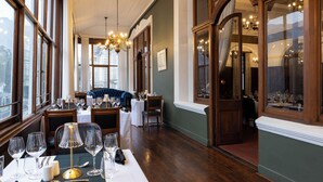 A dining area with tables set for a meal, large windows, and a chandelier. - The Cape Town Club (Cape Town)