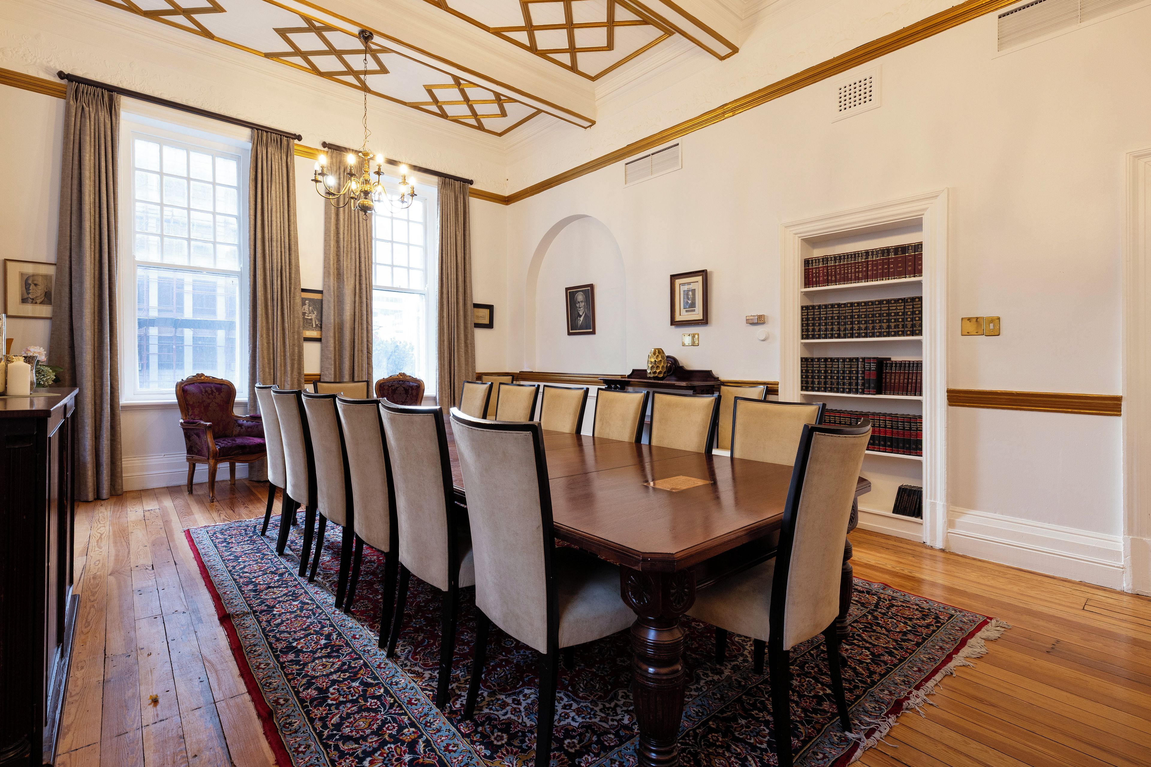 Un comedor formal con una mesa de madera, sillas tapizadas, un sendero con diseño y una estantería llena de libros.