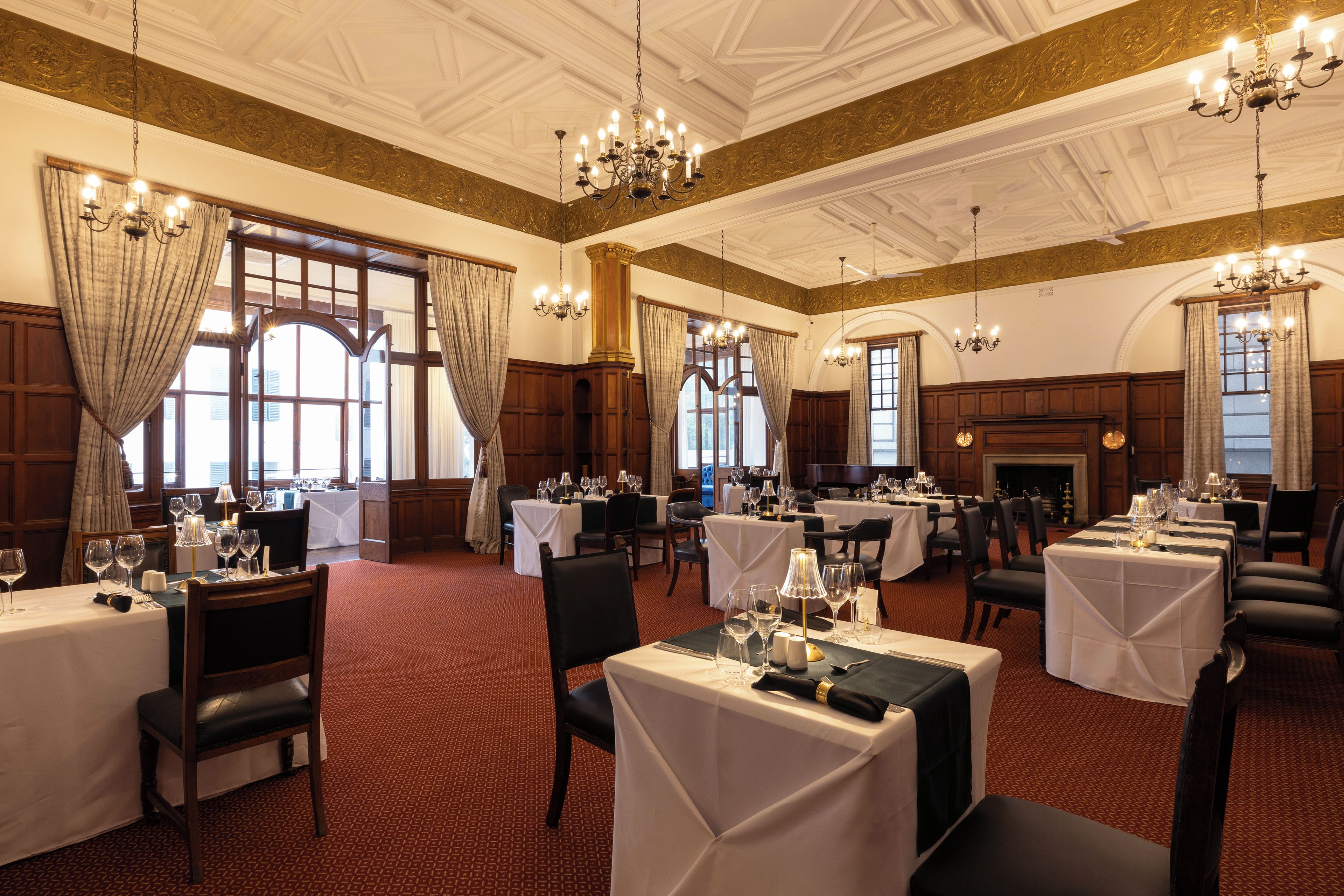 Un comedor formal con varias mesas dispuestas para el servicio, amplias ventanas con cortinas y detalles ornamentales en el techo.