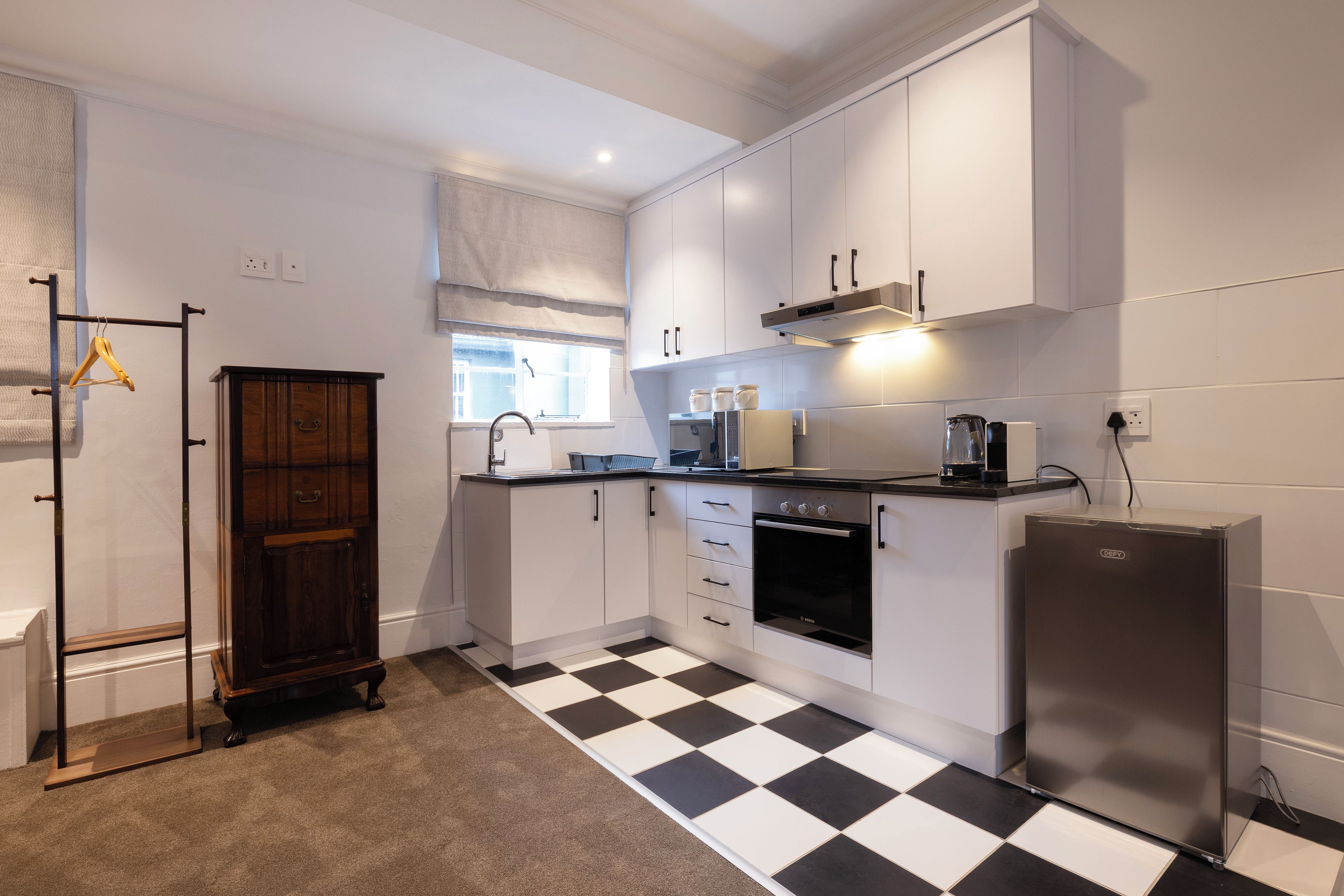 Una cocina moderna con armarios blancos, piso a cuadros blanco y negro, horno empotrado y refrigerador de acero inoxidable.