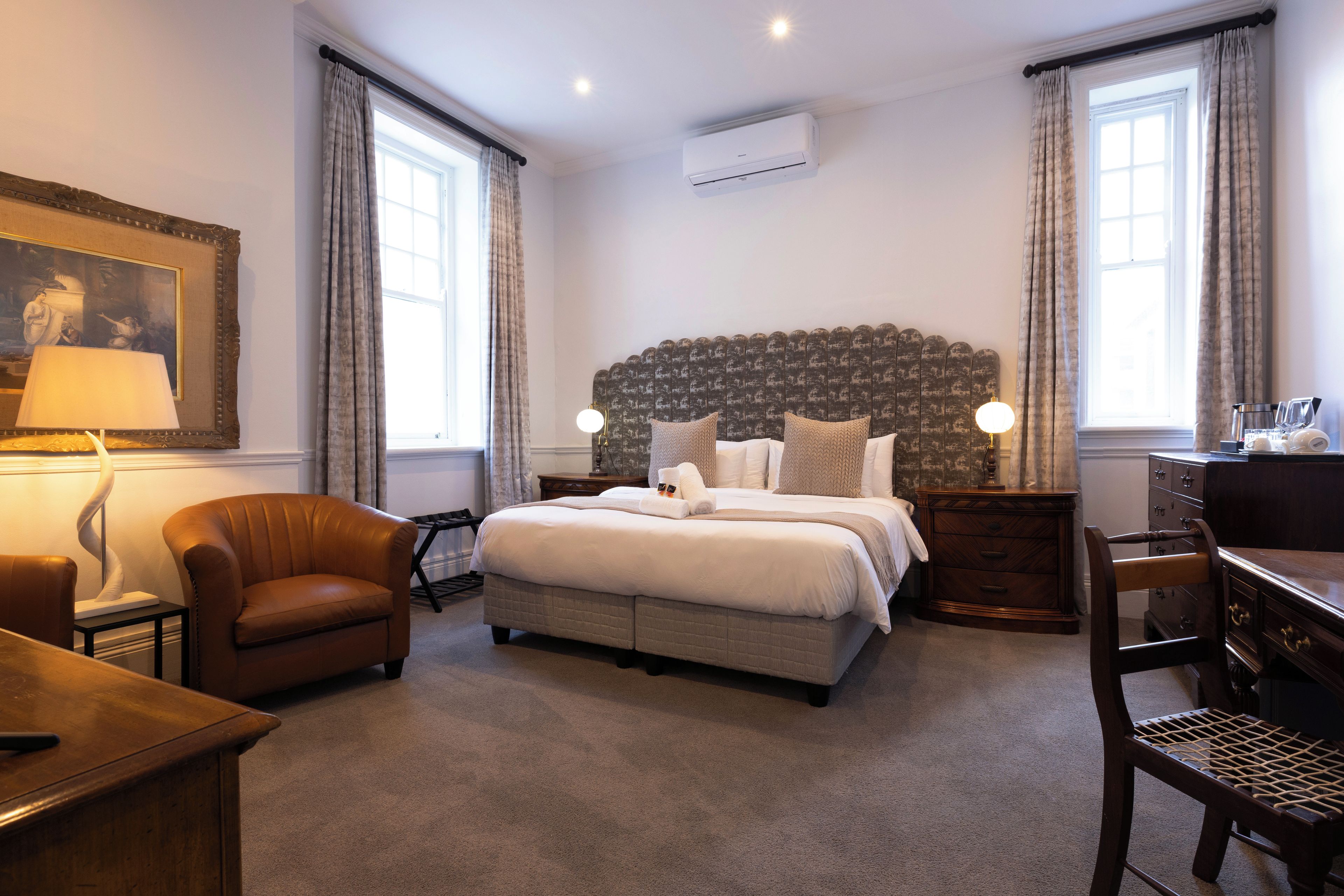 Ein Hotelzimmer mit einem großen Bett, einem Schreibtisch, einem Sessel, einer Lampe und einem Gemälde an der Wand.