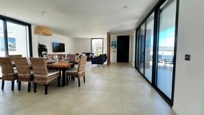 Amplia sala de estar con mesa de comedor, sillas de mimbre, televisor de pantalla plana y un gran ventanal corredero que da a un patio exterior.