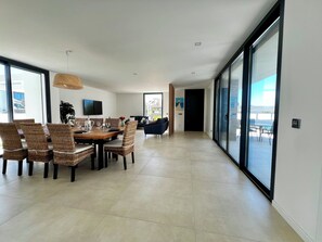 A spacious living area with a dining table, wicker chairs, a flat-screen TV, and a large sliding glass door leading to an outdoor patio.