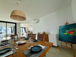 A dining area with a wooden table set for four, a wicker pendant light, and a painting on an easel.