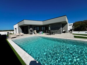 A modern house with a swimming pool, outdoor seating, and a view of the landscape.