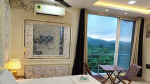 Una habitación de hotel con cama, ventana con vistas a la vegetación, ventilador de techo y aire acondicionado.
