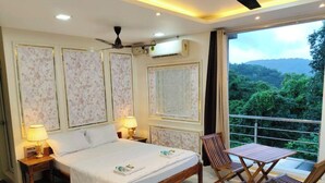 Un dormitorio con cama, mesitas de noche, ventilador de techo, equipo de aire acondicionado y un balcón con vistas a zonas verdes.