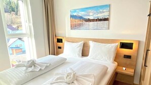 A hotel room with a bed, two bedside tables, a painting on the wall, and a window with a view of a building.