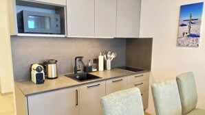 A compact kitchen with a microwave, kettle, coffee maker, and utensils on the counter. There are two chairs and a small table.