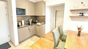 Una cocina compacta con microondas, pileta y electrodomésticos en la encimera. Hay una zona de comedor con una mesa de madera y dos sillas.