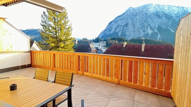 Un balcón con baranda de madera, una mesa y sillas, con vistas a un paisaje montañoso.