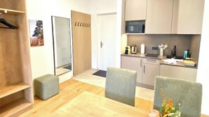 Una cocina moderna con armarios, microondas y una encimera. Se ve un mueble de madera a la izquierda y una zona de estar con mesa y sillas.