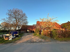 A rural barn with a dirt driveway leading to a gated entrance, surrounded by trees and open fields. - An‘n Feldkamp – Ferienwohnung auf dem Bauernhof (Emsdetten)