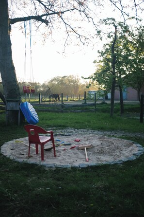 A circular sandpit with a red chair, a blue mat, and a swing set in the background. - An‘n Feldkamp – Ferienwohnung auf dem Bauernhof (Emsdetten)