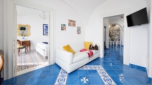 A room with a white sofa, blue patterned floor, a chandelier, a flat-screen TV, and artwork on the wall. - In the center of Amalfi, a dream home with a sea view! (Amalfi)