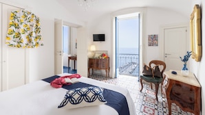 A hotel room with a bed, a chair, a desk, a TV, a chandelier, a balcony with a railing, and a door leading outside. - In the center of Amalfi, a dream home with a sea view! (Amalfi)