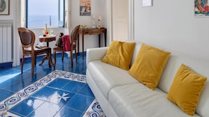 A room with a white sofa, a chandelier, a dining table with chairs, a window with a view, and a patterned floor. - In the center of Amalfi, a dream home with a sea view! (Amalfi)