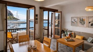 A room with a wooden table, chairs, a sofa, and a view of a marina with boats. - Matroni's House - Seafront Getaway in Monemvasia (Gefira)