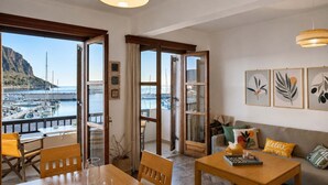 A room with a view of a marina, a wooden table, a sofa, and framed artwork on the wall. - Matroni's House - Seafront Getaway in Monemvasia (Gefira)