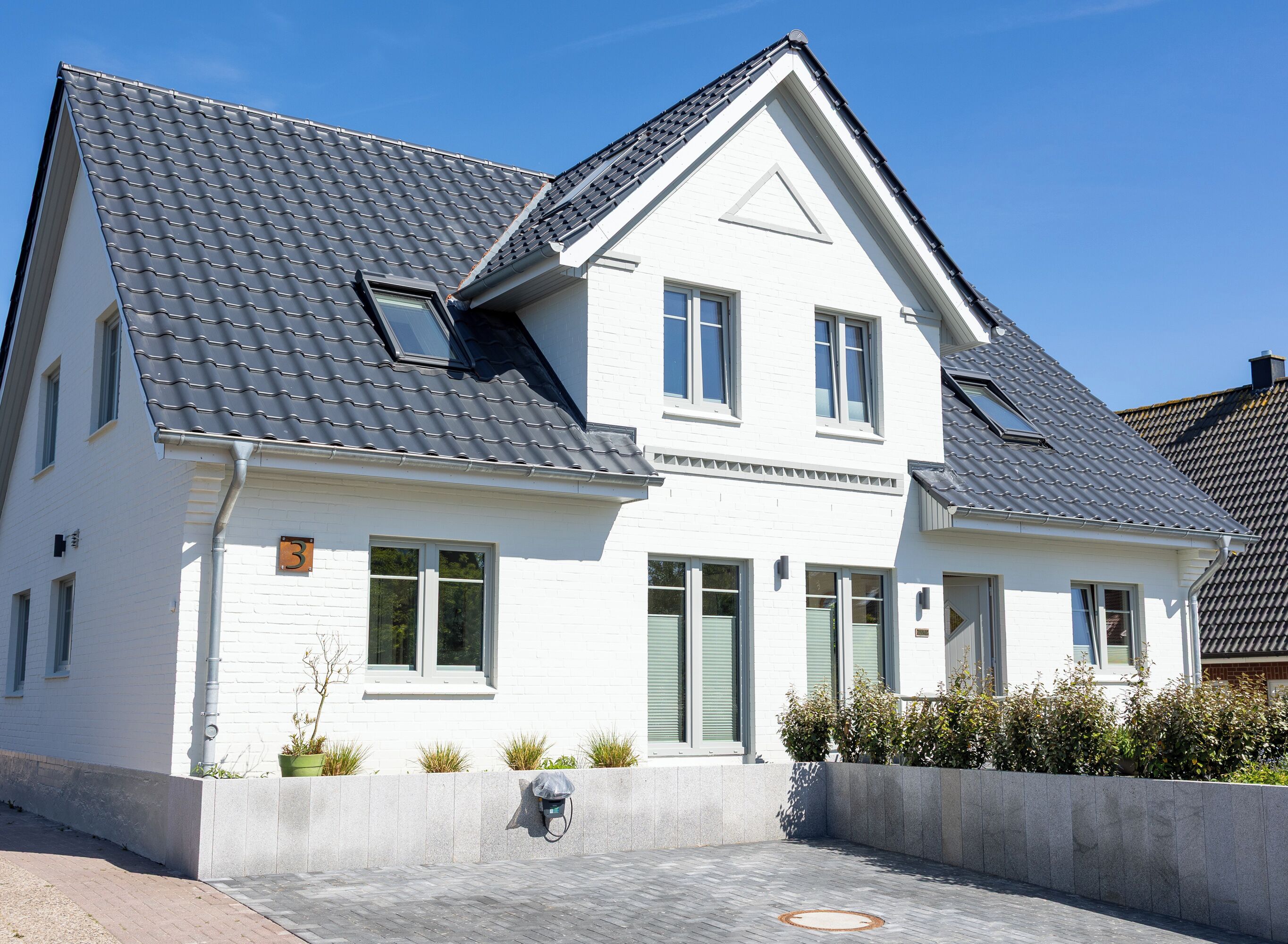 A two-story house with a grey tiled roof, white exterior walls, and a small front garden.