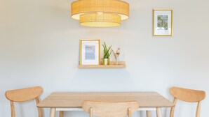 Un comedor con una mesa de madera, dos sillas, una lámpara colgante y dos elementos decorativos en la pared.