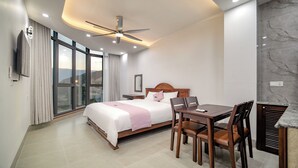 Une chambre d’hôtel moderne équipée d’un lit, d’une table à manger avec des chaises, d’un ventilateur de plafond et d’une grande fenêtre.