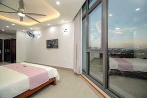 Ein modernes Hotelzimmer mit einem großen Bett, Deckenventilator und einem großen Fenster mit Blick auf die Stadt.