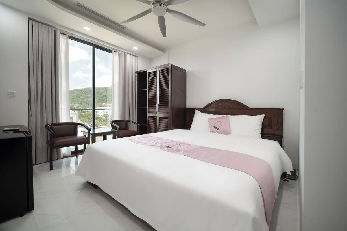 Ein Hotelzimmer mit Bett, Schreibtisch, Stuhl, Kleiderschrank und Blick ins Freie.