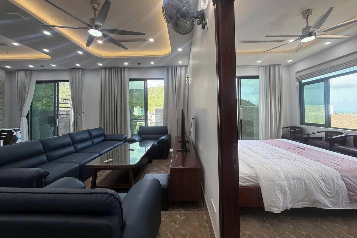 Ein modernes Hotelzimmer mit einer Couch, einem Bett, einem Esstisch und zwei Deckenventilatoren.