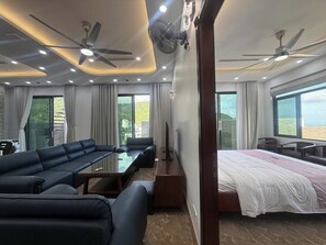 Ein modernes Hotelzimmer mit einer Couch, einem Bett, einem Esstisch und zwei Deckenventilatoren.
