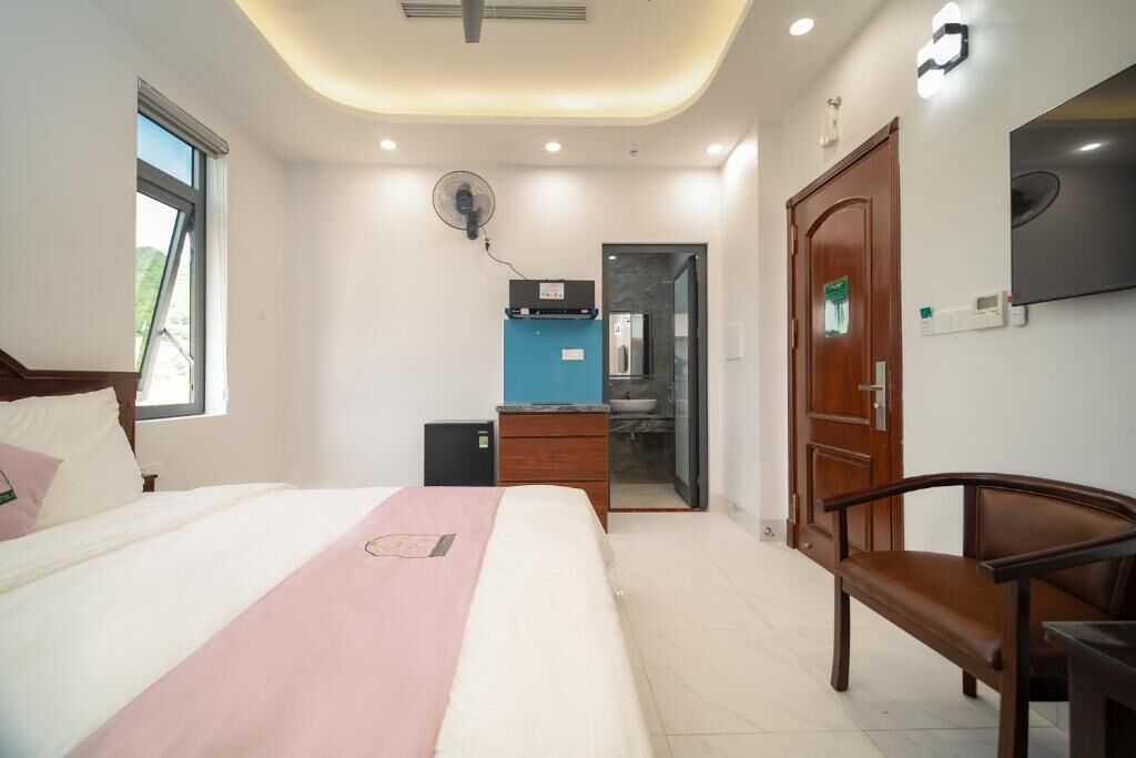 Un dormitorio con cama, escritorio, silla, armario, televisor y baño visible a través de una puerta abierta.