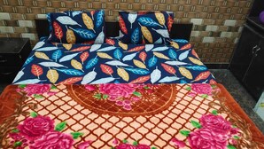 A bed with a patterned bedspread and pillows, a decorative rug with floral designs, and a wooden headboard.