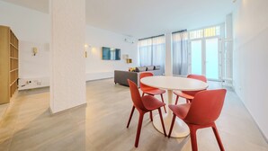 Een moderne woonkamer met een ronde tafel, rode stoelen, een grijze bank en een televisie.
