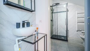 Een moderne badkamer met een douchecabine van glas, een wit wastafelmeubel met een glazen blad en een spiegel boven de wastafel.