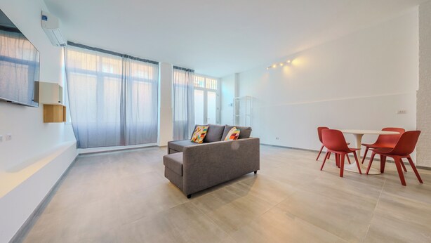 Een moderne woonkamer met een grijze bank, rode stoelen en een eettafel.