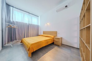 Een slaapkamer met een bed, nachtkastjes, een kledingkast, een droogrek en een raam met gordijnen.