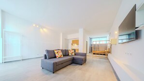 Een moderne woonkamer met een grijze hoekbank, een aan de muur bevestigde televisie en een trap naar een hoger niveau.