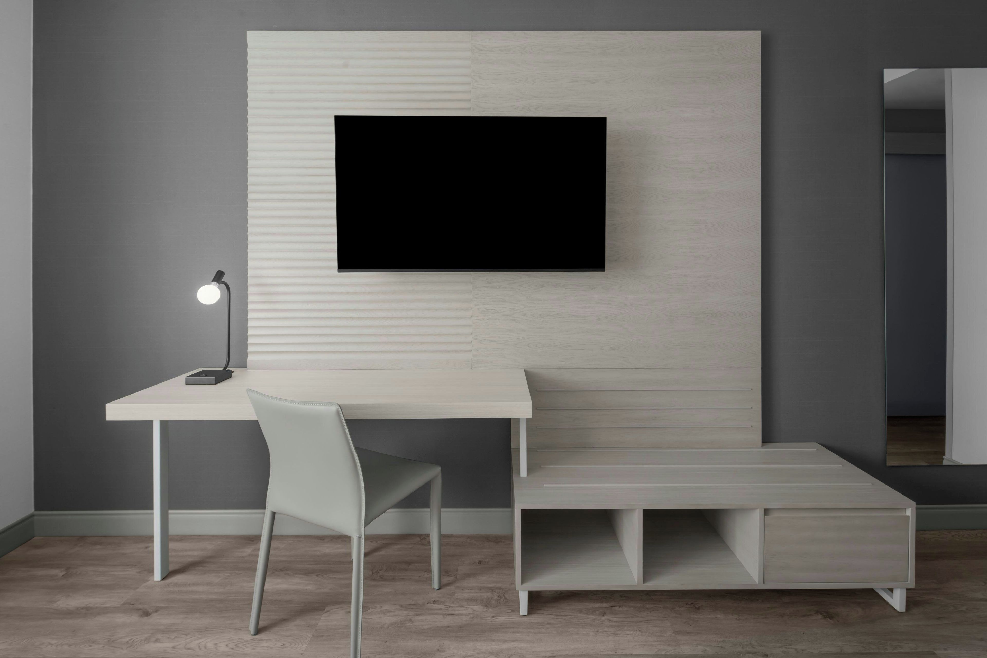Una habitación moderna con escritorio, silla y televisión montada en la pared.