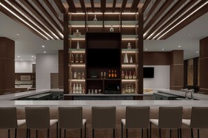 Un área de bar moderna con una barra larga, diversas opciones de asientos y una variedad de botellas y vasos a la vista.