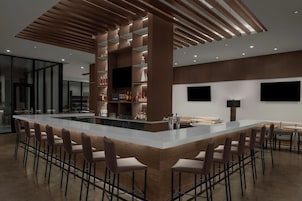 Zona de bar moderna con una isla central, taburetes y una pantalla de televisión.